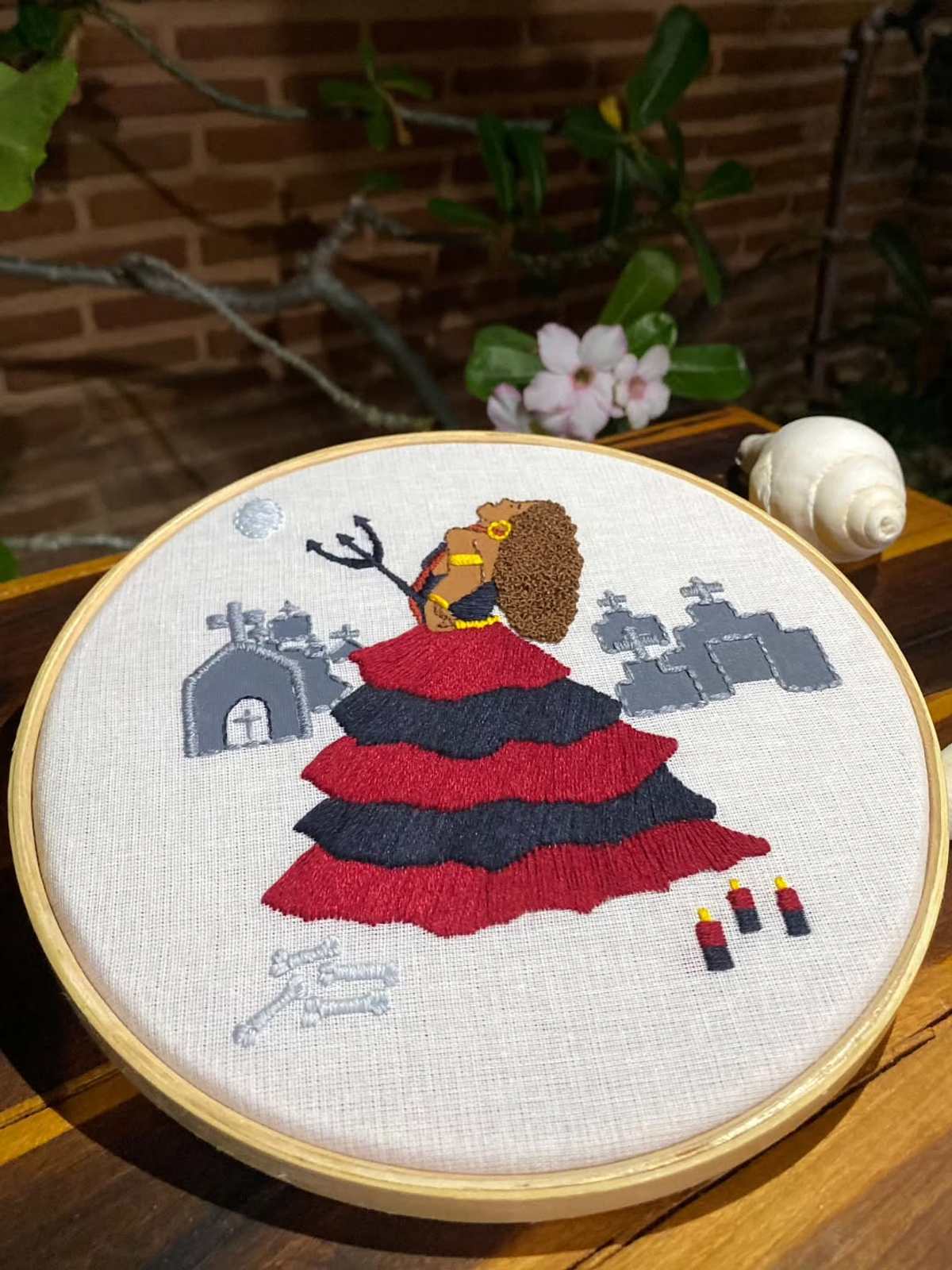 Bastidor com Maria Mulambo de saia vermelha e preta diante de cruzes