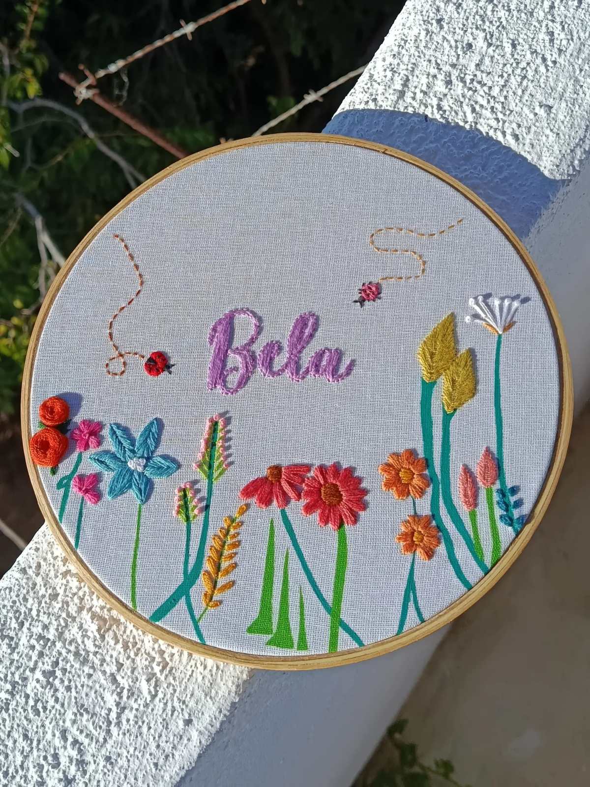 Bastidor com um nome bordado em rosa entre flores coloridas