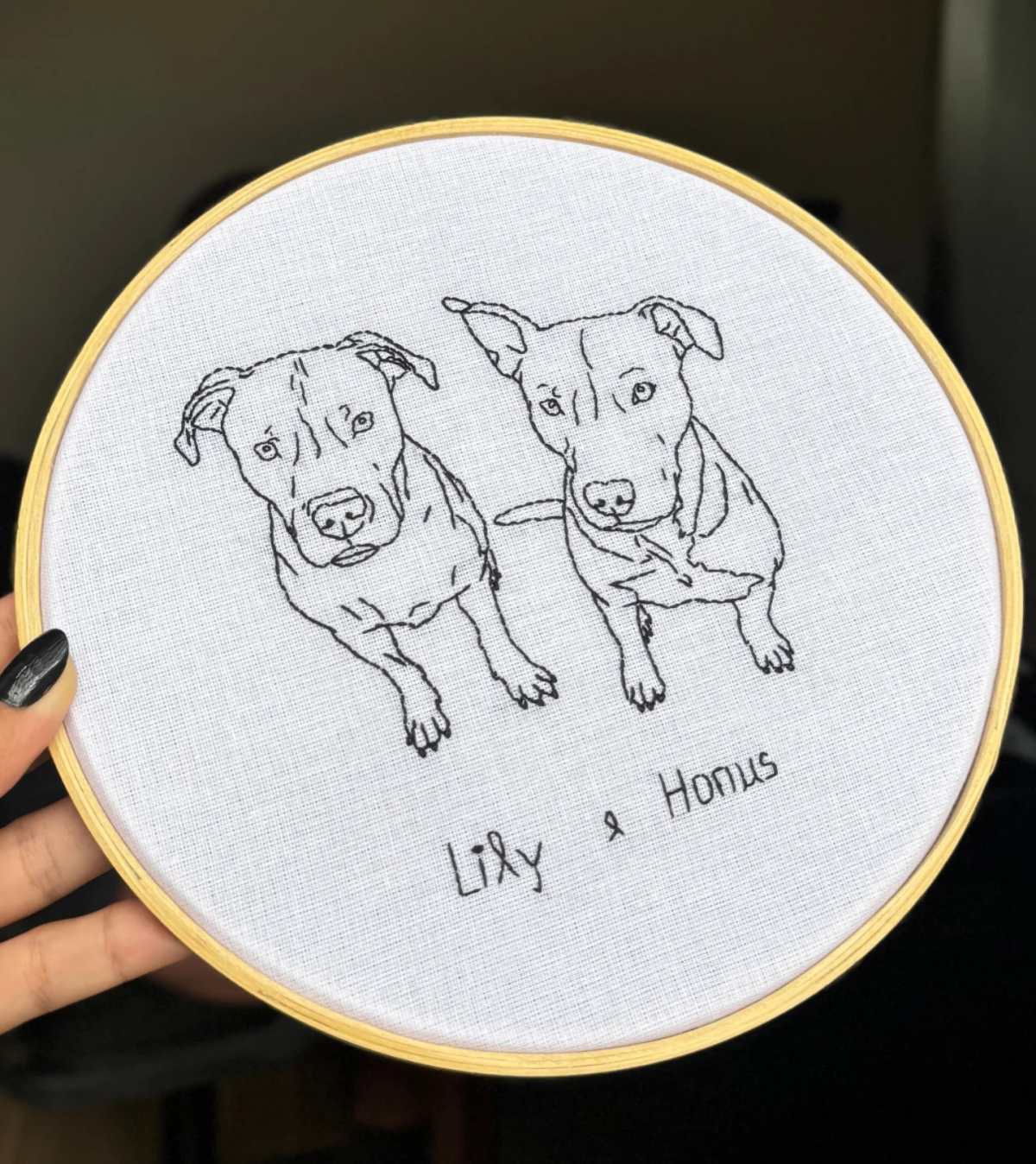 Bastidor com dois cachorros bordados em linha preta, cada um com o seu nome